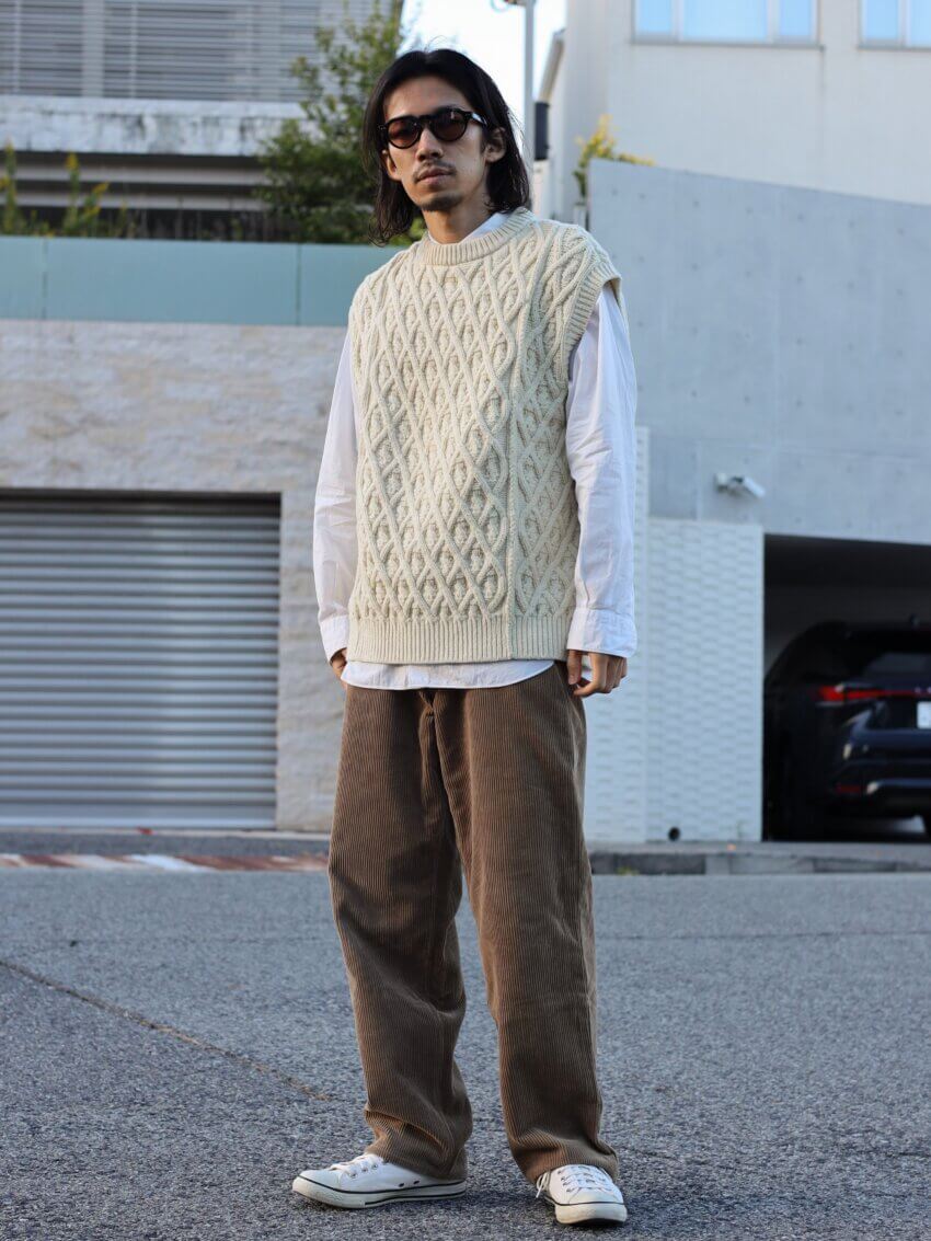 オーラリーのニットベストとコーデュロイパンツ、コモリのシャツ、コンバースのオールスター、ユニクロのサングラスのメンズコーデ